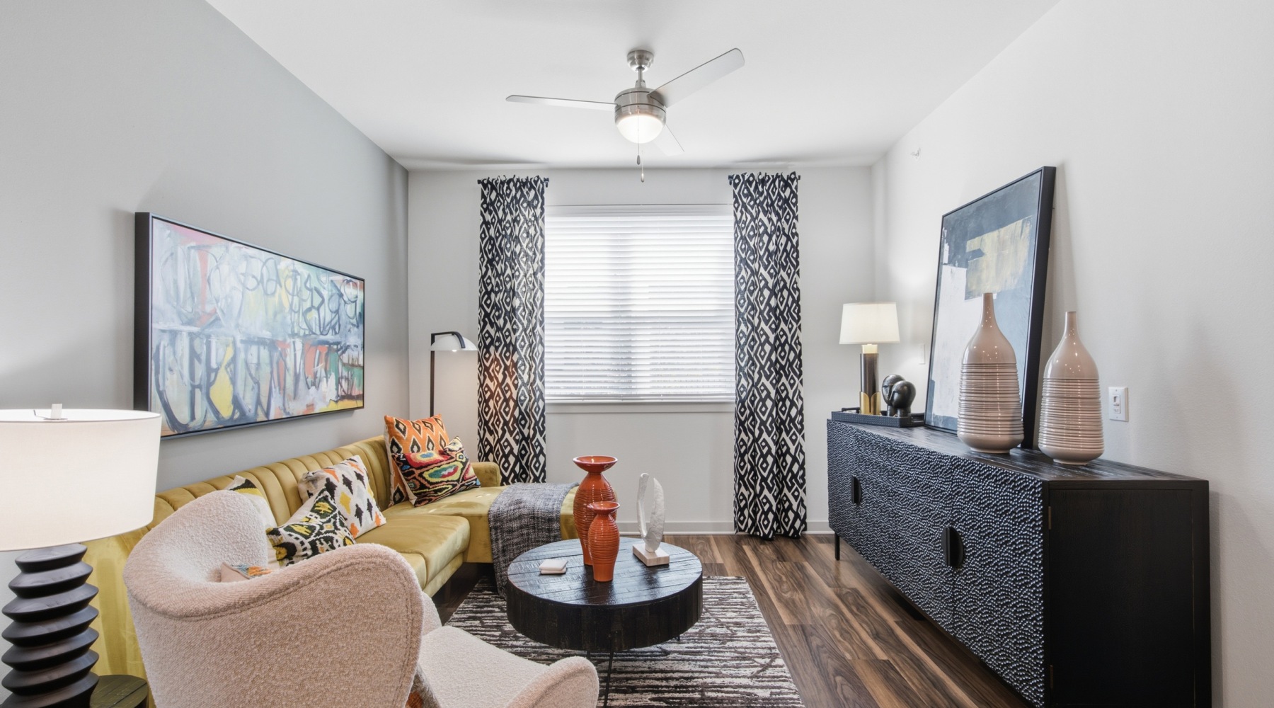 Model living room at our apartments for rent in Aubrey, TX, featuring wood grain floor paneling and windows with curtains.
