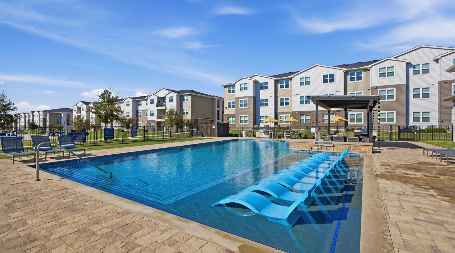 Pool area at our apartments for rent in Aubrey, TX, featuring beach chairs, umbrellas, and a clubhouse.