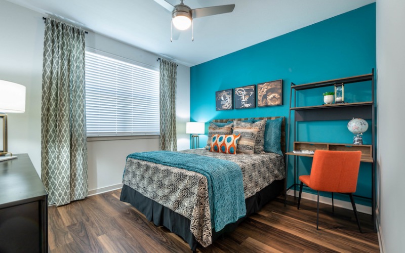 Model bedroom at our apartments for rent in Aubrey, TX, featuring wood grain floor paneling and windows with blinds.