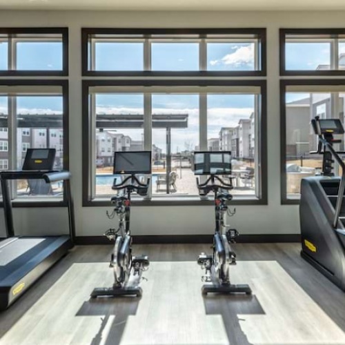 The fitness center at our apartments in Aubrey, featuring wood grain floor paneling, treadmills, and stair steppers.